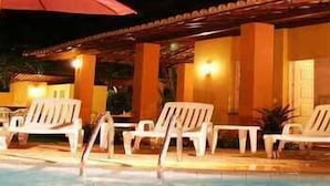 A pool area with white lounge chairs and a red umbrella. - Villa Flamboyan (Lauro de Freitas)