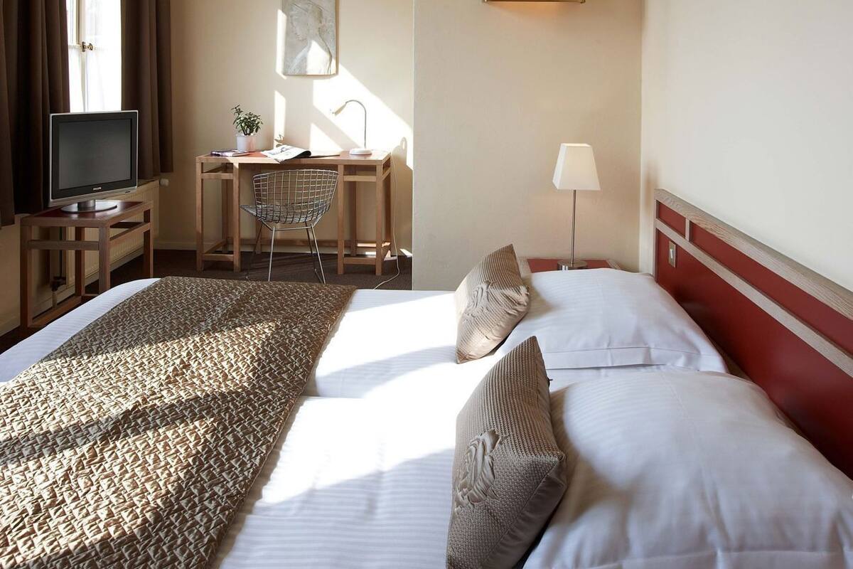 A hotel room with a bed, a desk, a chair, a television, and a window.