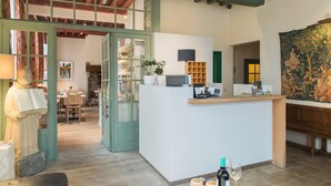 A reception area with a counter, a statue, a painting, and a view into a dining area. - Hotel Adornes (Bruges)