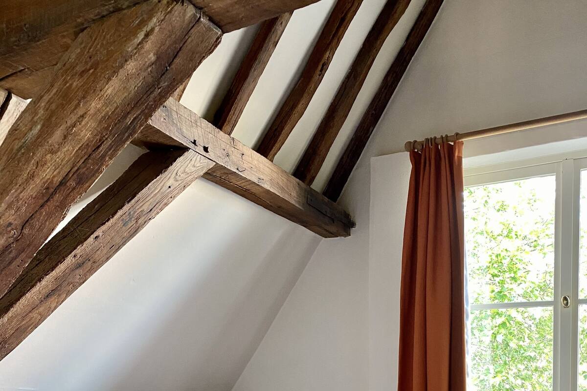 A bedroom with a sloped ceiling, a bed with a red blanket, and a window with curtains.