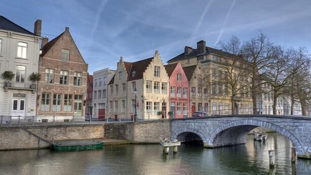 A stone bridge over a calm river with historic buildings on either side. - Hotel Adornes (Bruges)