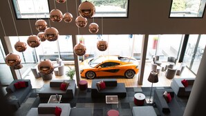 Un'area lounge moderna con divani, tavolini e un'auto visibile dalla finestra.