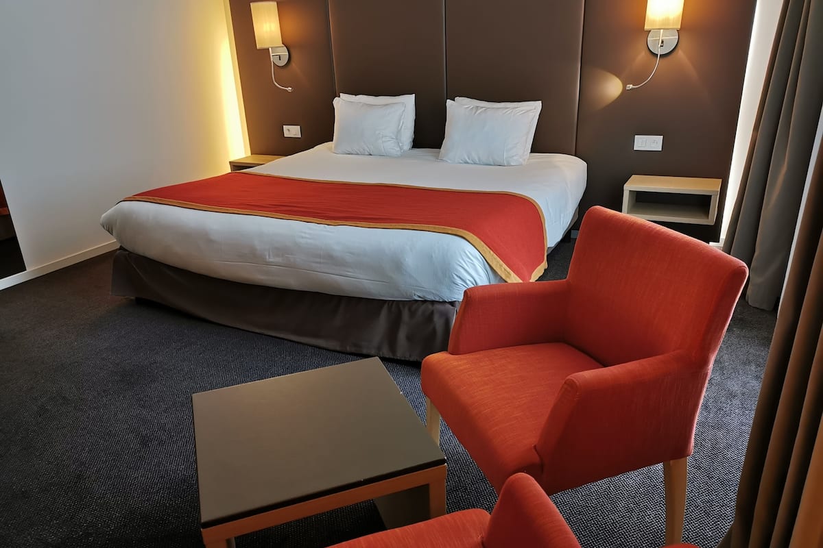 A hotel room with a bed, two bedside tables, a chair, and a small table.