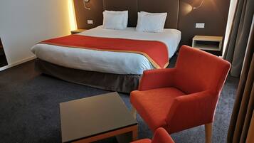 Una habitación de hotel con una cama, dos mesitas de noche, una silla y una pequeña mesa.