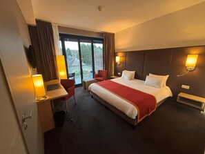 Une chambre d’hôtel avec un grand lit, un bureau avec une chaise, une petite table et une fenêtre avec des rideaux.