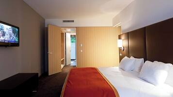 Une chambre d’hôtel avec un lit, un téléviseur fixé au mur et une porte donnant sur un couloir.