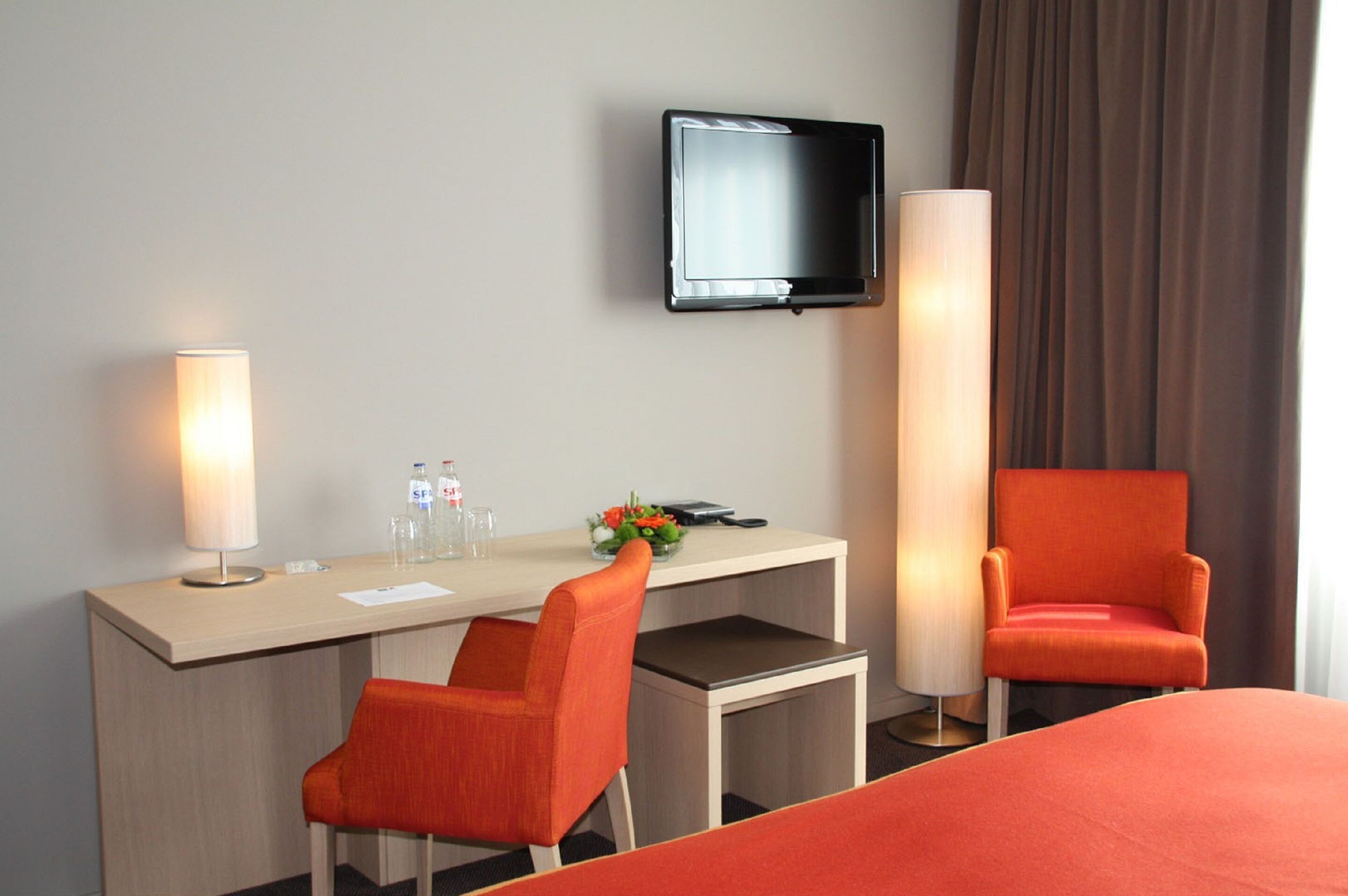 Ein Hotelzimmer mit Schreibtisch, zwei Stühlen, Fernseher, Lampe und Bett.