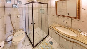 A modern bathroom with a glass shower enclosure, a white toilet, and a granite sink with a mirror above it.
