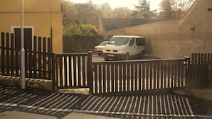 A gated parking area with a white van parked inside, surrounded by a wooden fence and a yellow building. - Diamant- Guest House (Karlovy Vary)