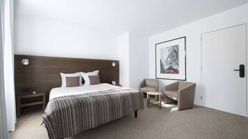 Ett modernt hotellrum med en stor säng, en sänggavel, ett nattduksbord, en stol, ett litet bord och ett inramat konstverk på väggen.