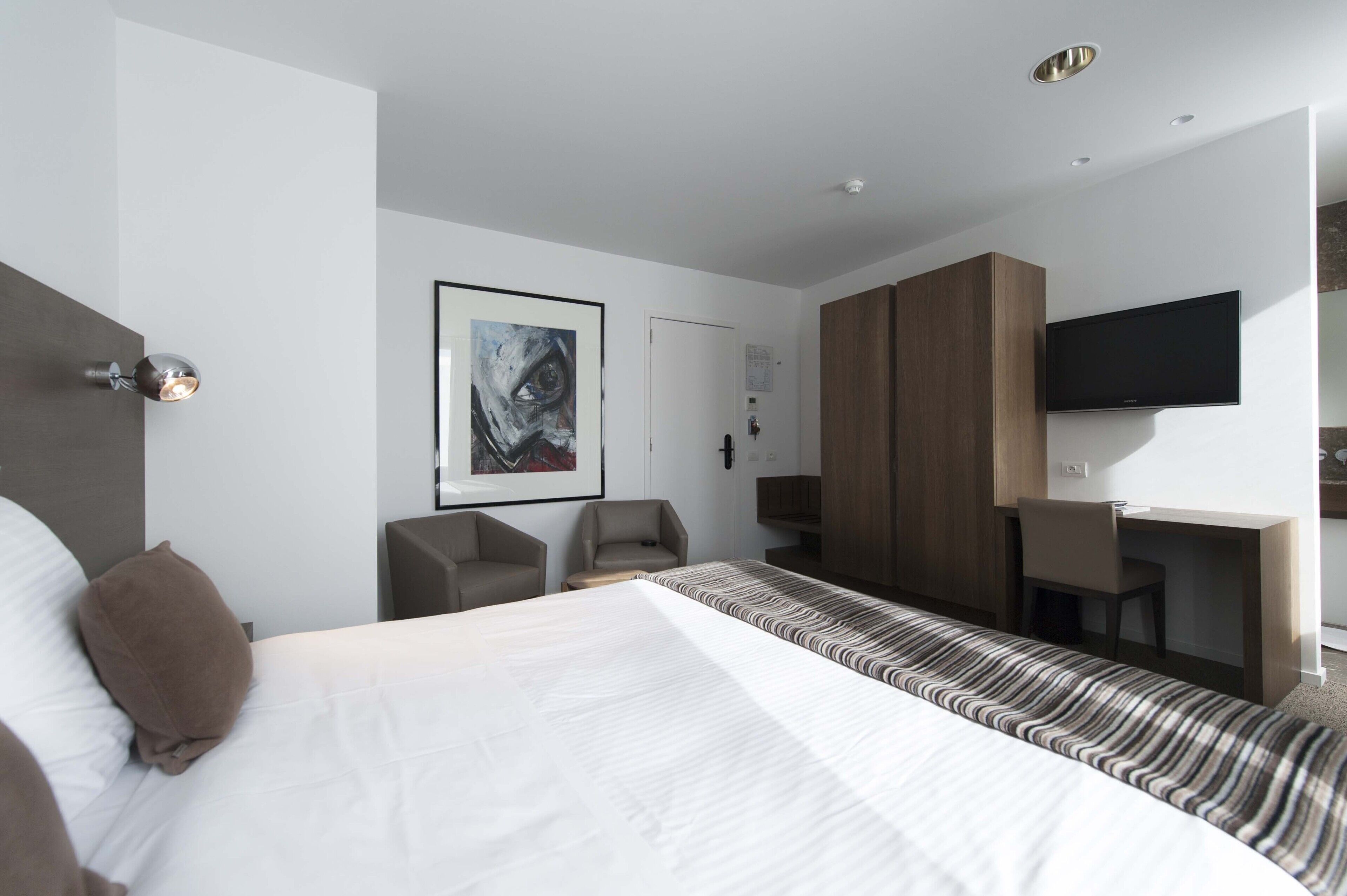 A modern hotel room with a large bed, a desk, a chair, and a TV.