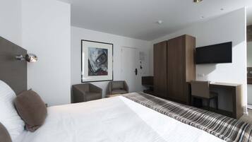 A modern hotel room with a large bed, a desk, a chair, and a TV.