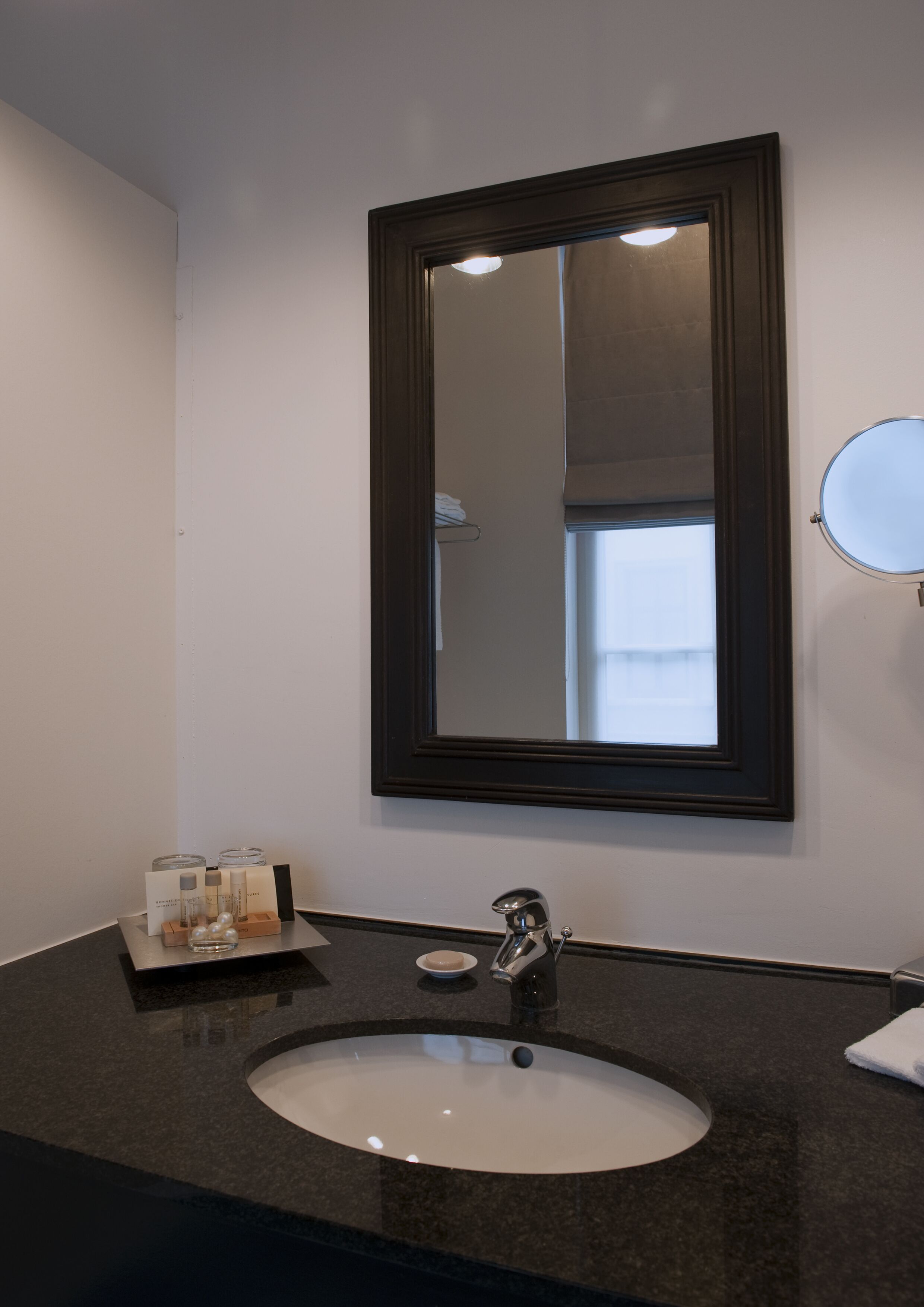 A bathroom with a large mirror, a sink, and a small round mirror on the wall.