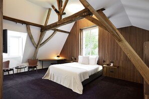 Un dormitorio con techo inclinado, una cama, un escritorio, dos sillas y una ventana.