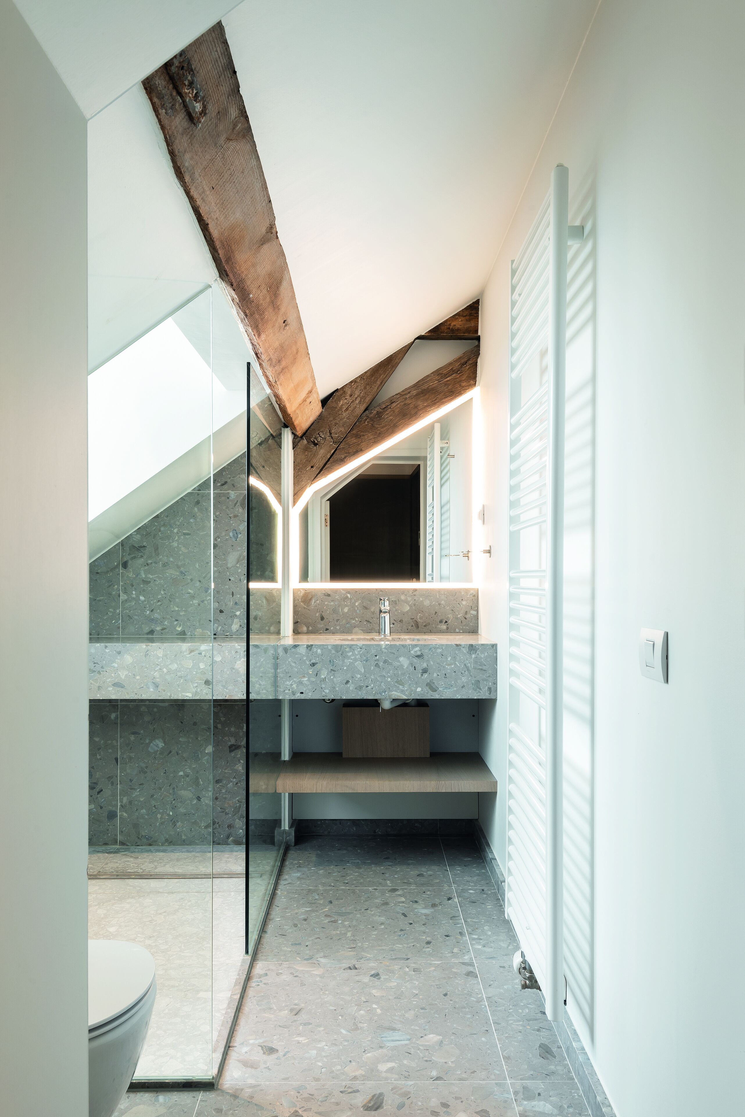 Un baño moderno con encimera de piedra, cabina de ducha de vidrio y techo con vigas de madera.