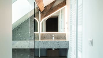 Un baño moderno con encimera de piedra, cabina de ducha de vidrio y techo con vigas de madera.