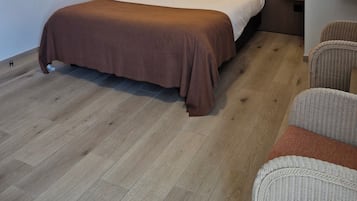Una habitación de hotel moderna con una cama grande, un cabecero con iluminación integrada, una obra de arte enmarcada en la pared y una silla de mimbre.