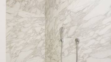 A bathroom with marble walls and a shower with a handheld showerhead.