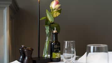 Une table dressée avec une bouteille de vin, un verre, un vase avec une fleur, des salières et des poivrières, et une lampe.