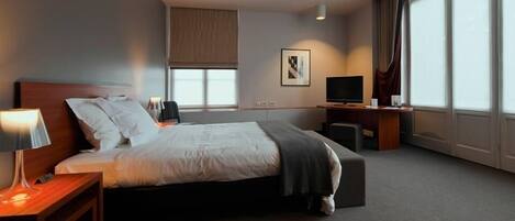 A hotel room with a bed, a desk, a television, and a window with curtains.