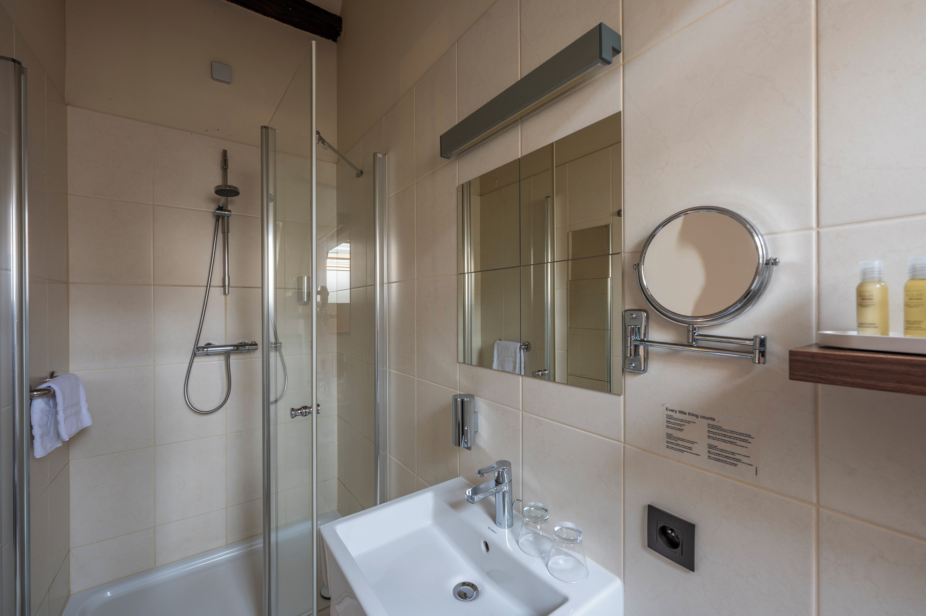 A modern bathroom with a glass-enclosed shower, a sink with a mirror, and toiletries on a shelf.