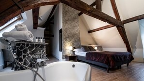 Un dormitorio con una cama grande, suelo de madera, baño con bañera y pared de piedra.