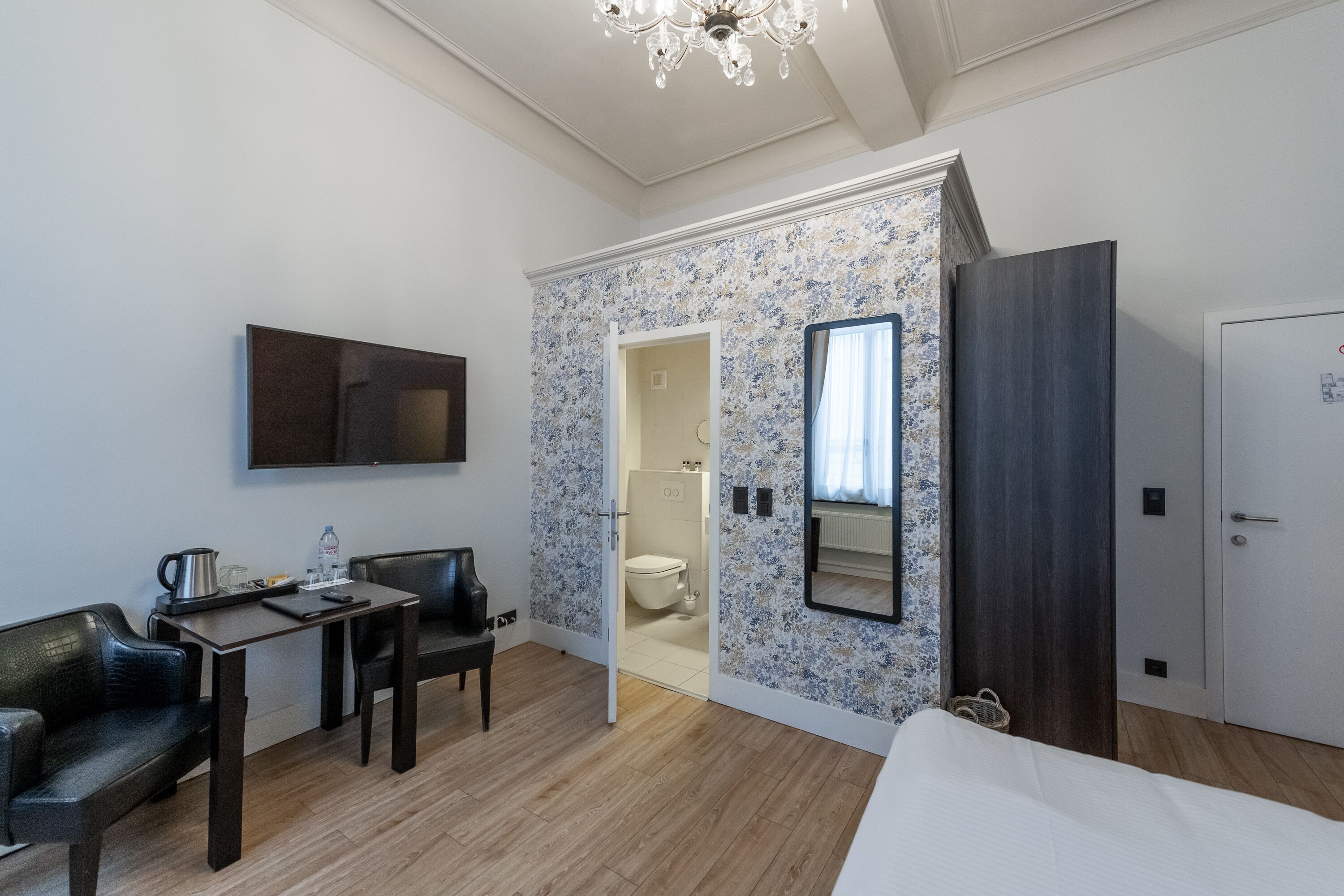 Een hotelkamer met een bed, een bureau met stoel, een televisie, een kledingkast en een badkamer die door een geopende deur zichtbaar is.