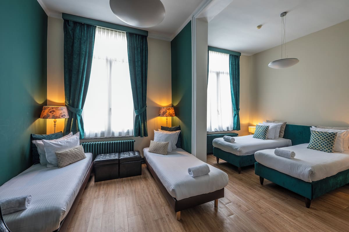 Habitación de hotel con dos camas individuales, un sofá, una mesita y una ventana con cortinas.