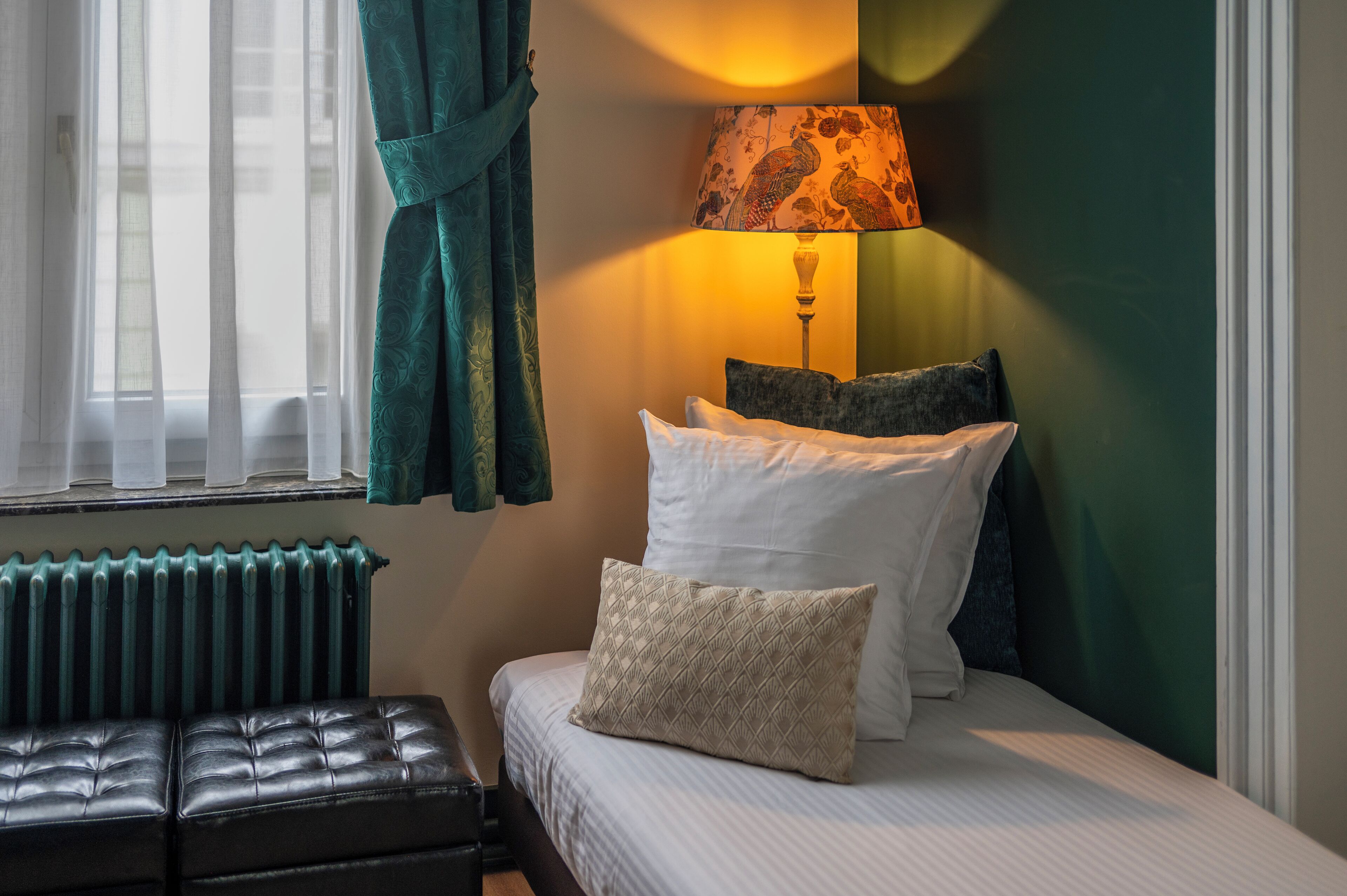 A neatly made bed with pillows, a bedside lamp, and a window with curtains.