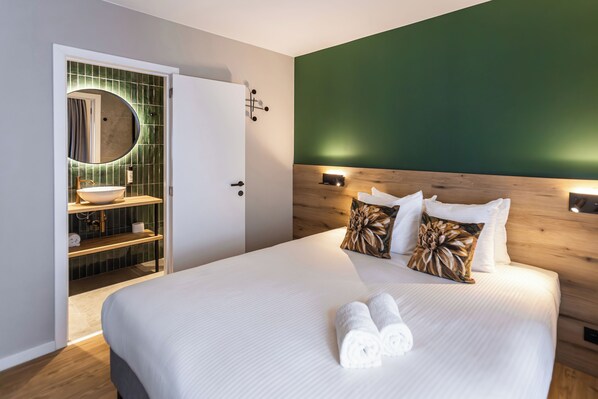 A modern hotel room with a large bed, a wooden headboard, a green accent wall, a round mirror, and a built-in sink with a wooden shelf. - Boutique Hotel Onderbergen (Ghent)