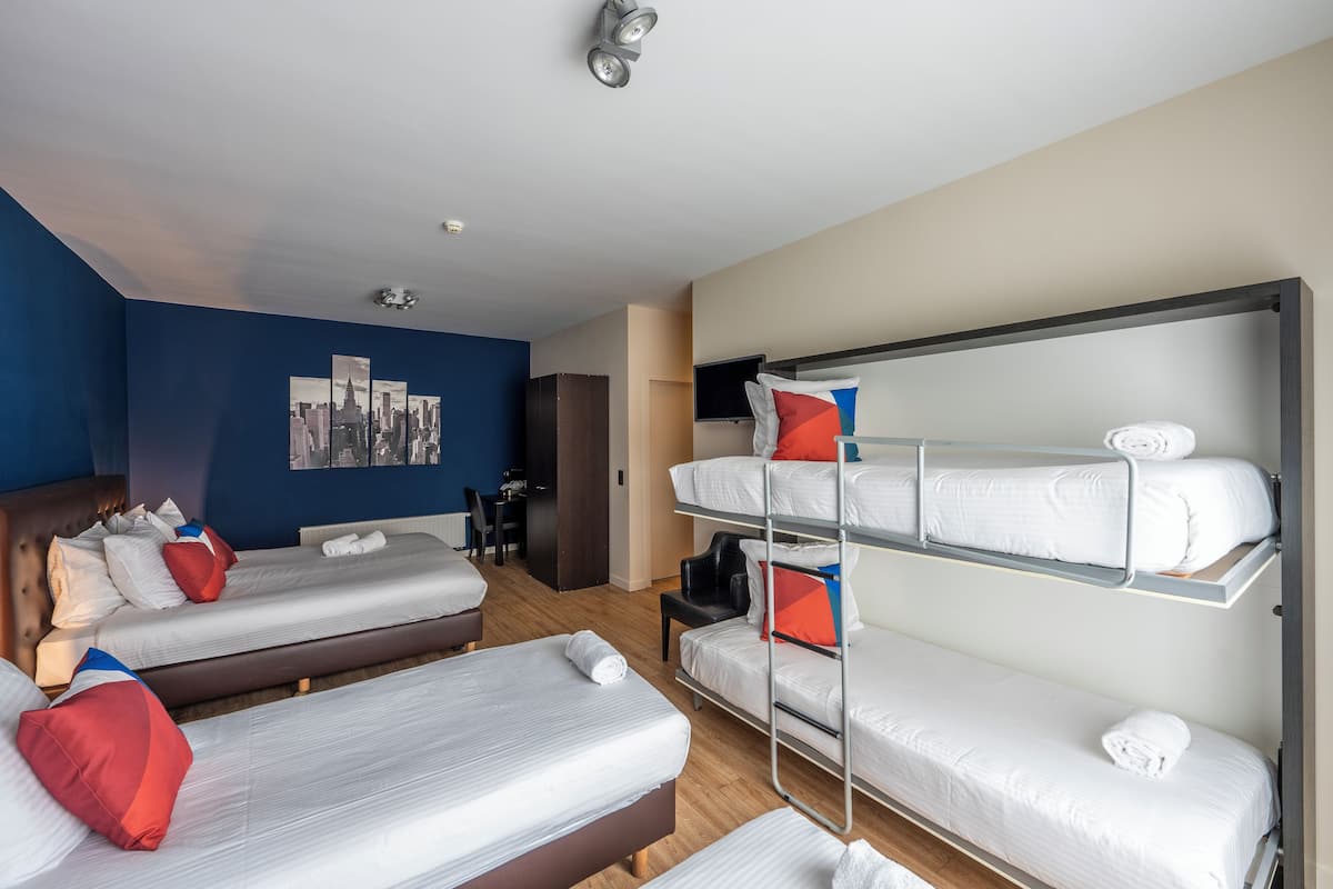 Habitación de hotel con dos camas individuales, una litera, un escritorio, una silla y un televisor.