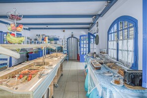 Ein Buffet mit verschiedenen Speisen, einer Kaffeemaschine und einem Essbereich mit blauer Tischdecke.
