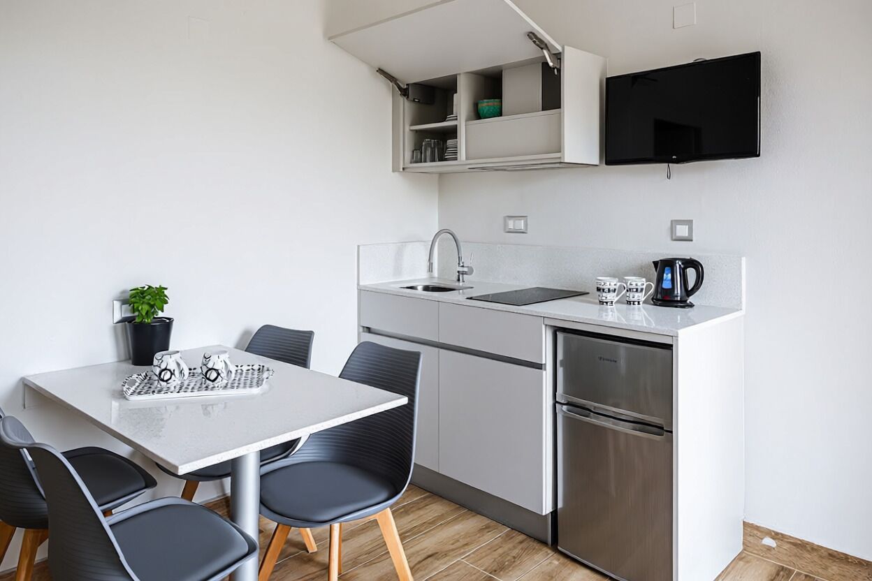 A compact kitchen with a built-in refrigerator, a sink, and a flat-screen TV mounted above the counter.