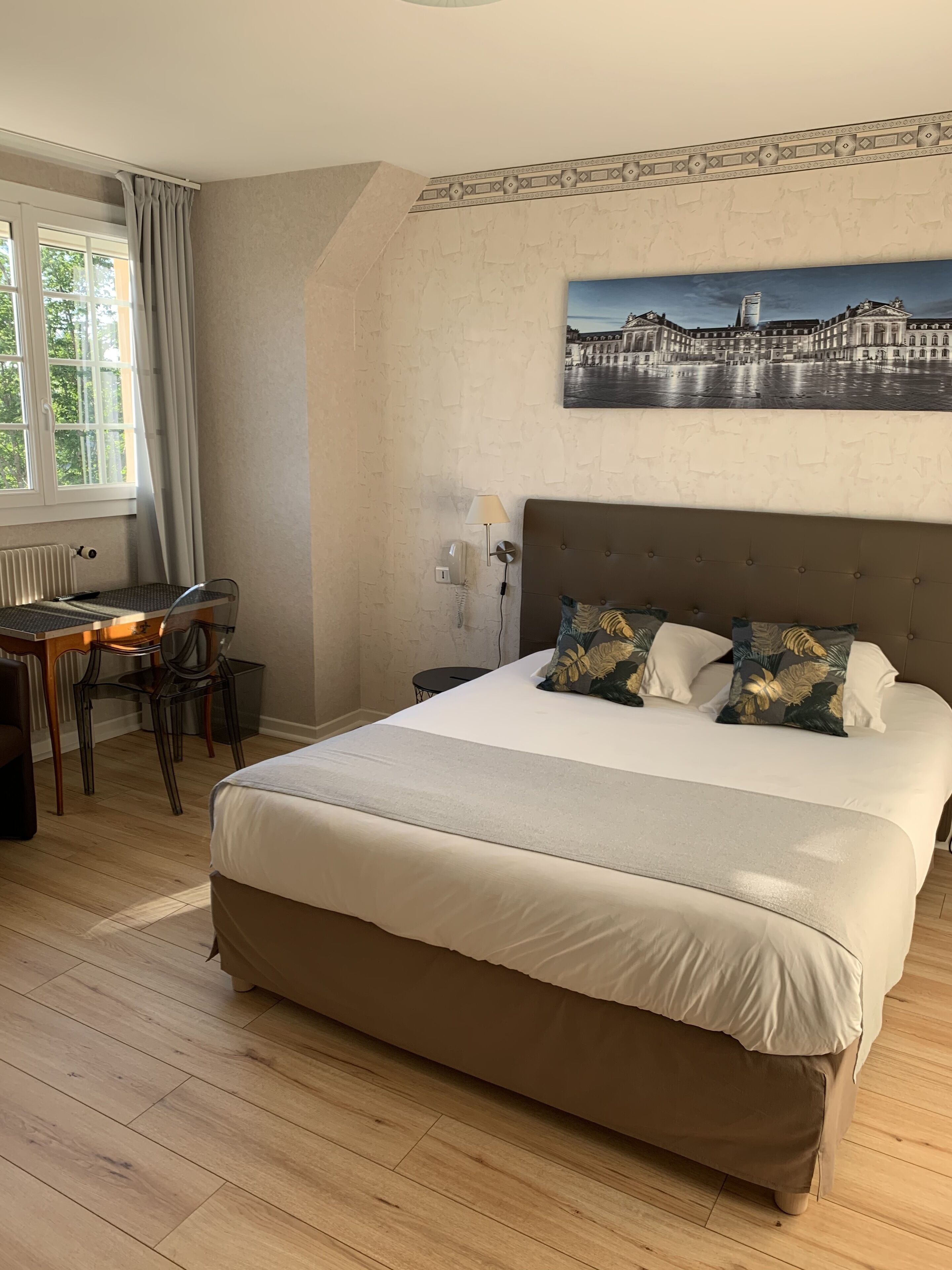 A bedroom with a large bed, a desk with a chair, a radiator, and a window with curtains.