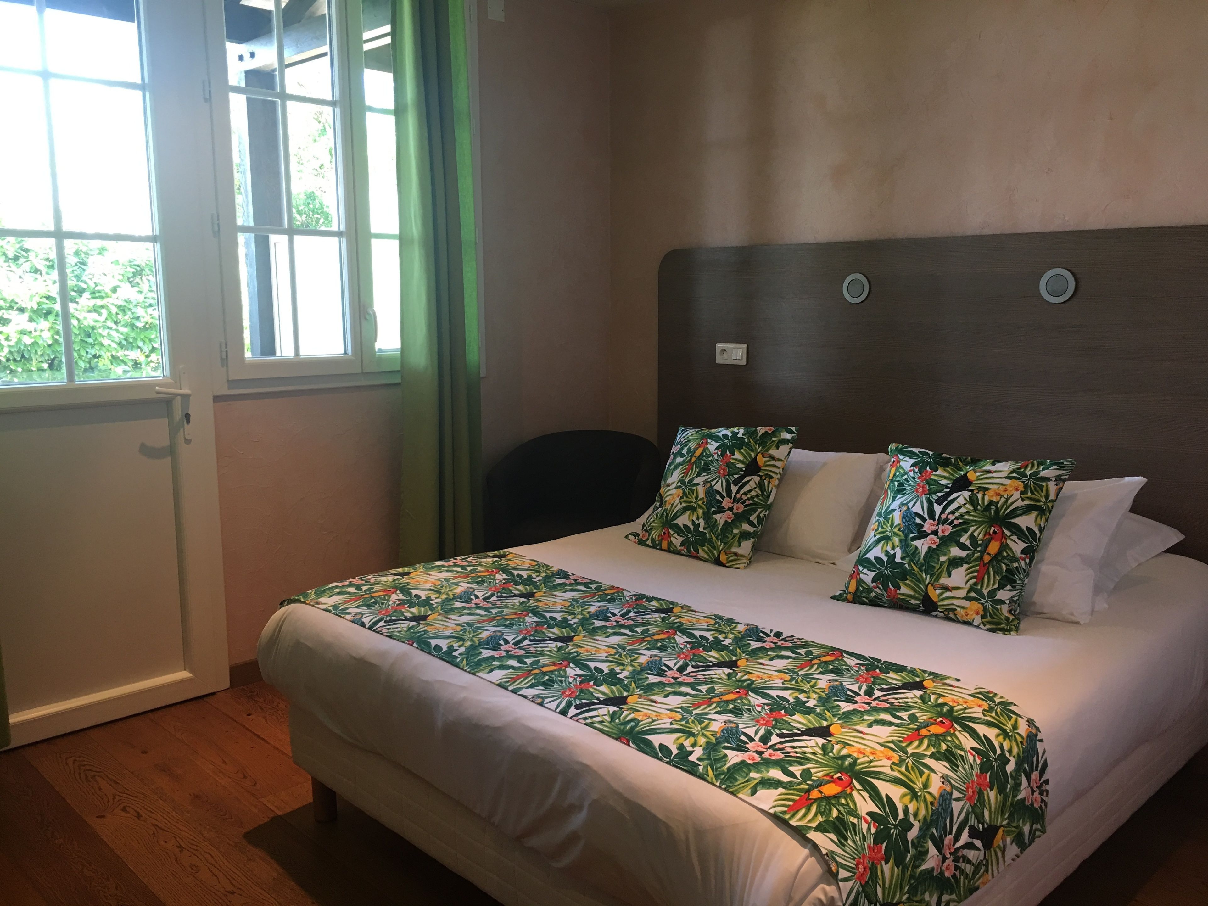 A hotel room with a large bed, a window with curtains, and a view of greenery outside.