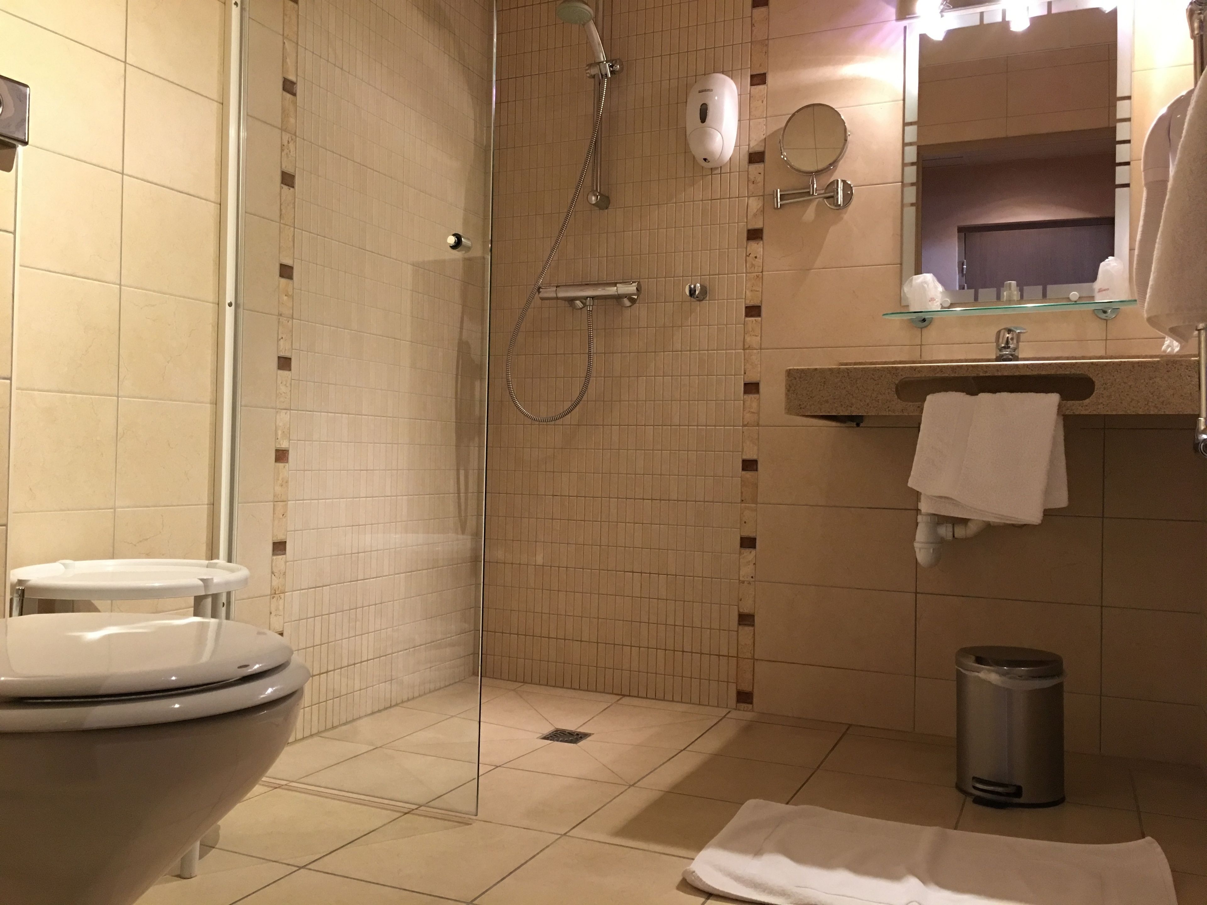 A bathroom with a toilet, a shower, a sink with a mirror, and a trash can.