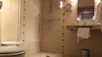 A bathroom with a toilet, a shower, a sink with a mirror, and a trash can.