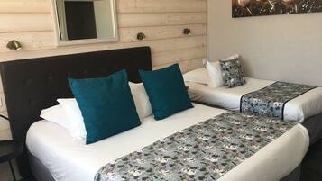 A hotel room with two beds, each with white bedding and teal pillows. There is a floral painting on the wall and a mirror above the beds.