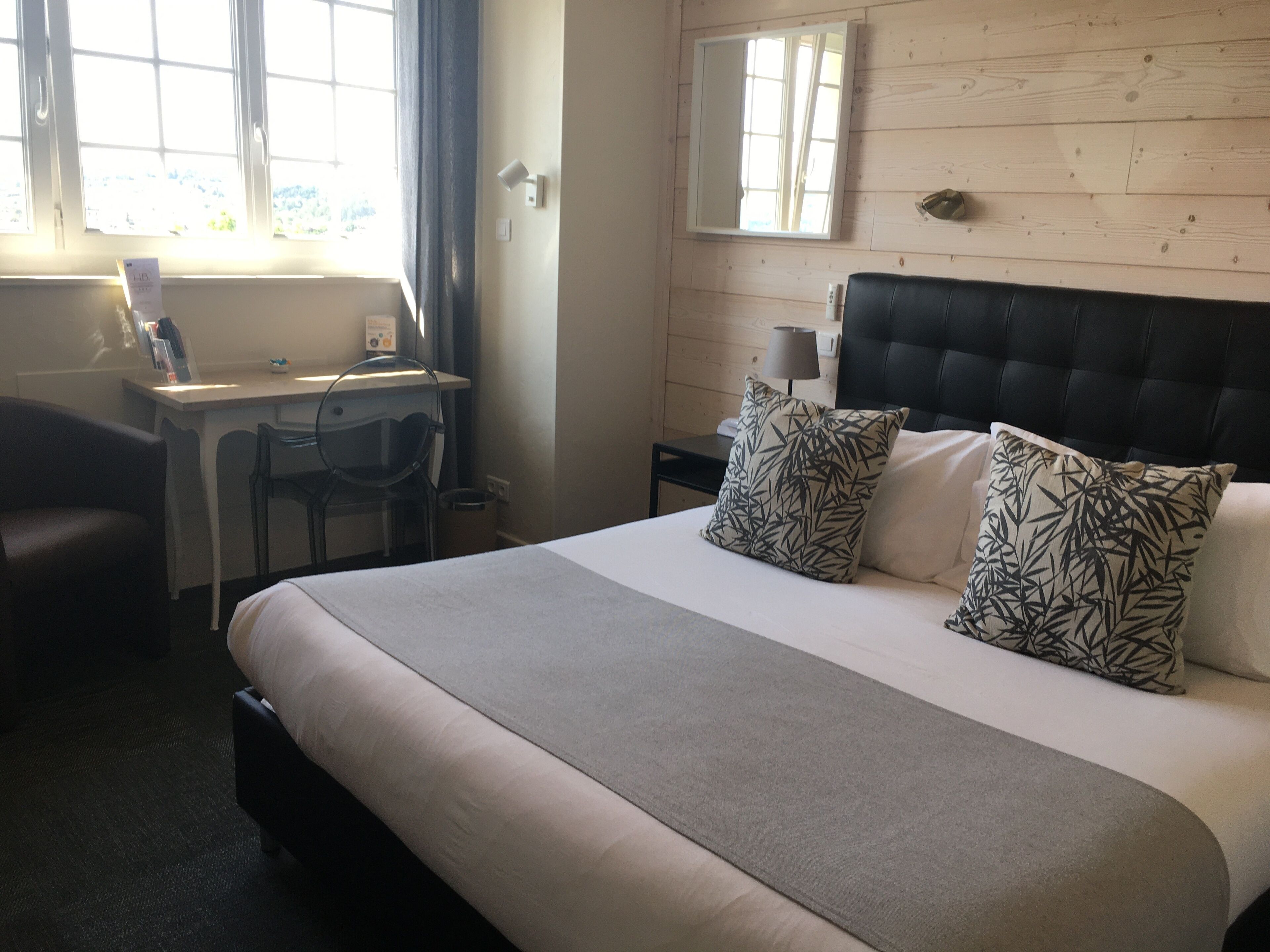 Een hotelkamer met een bed, bureau, stoel en een raam met gordijnen.