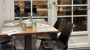A dining area with a table set for four, chairs, and a view through a glass door to an interior space. - La Bonbonniere, Sure Hotel Collection by Best Western (Talant)