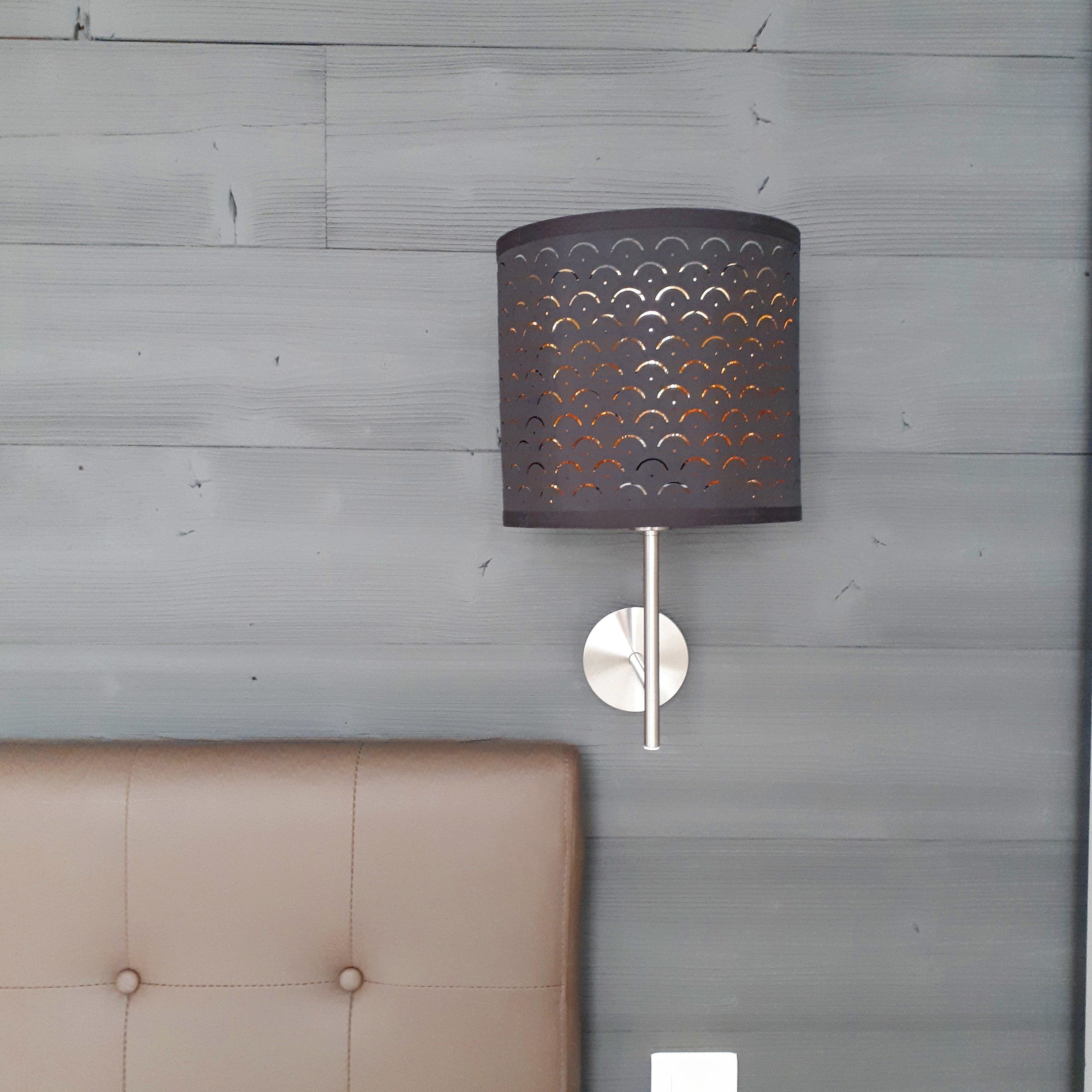 A wall-mounted lamp with a perforated metal shade and a round base on a wooden wall.