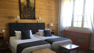 A double bed with a dark headboard, two bedside tables, a small wooden table, and a window with curtains.