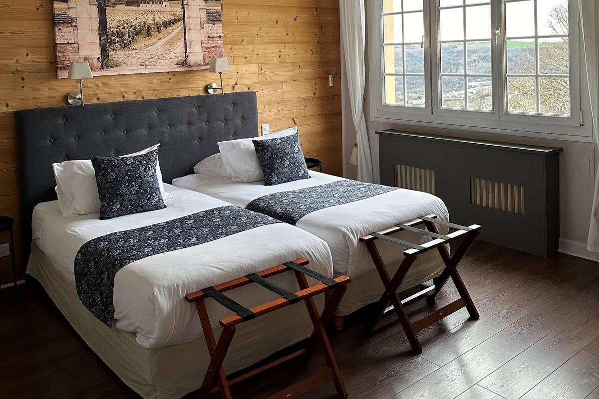 A bedroom with a large bed, a headboard, a window with curtains, and a painting on the wall.