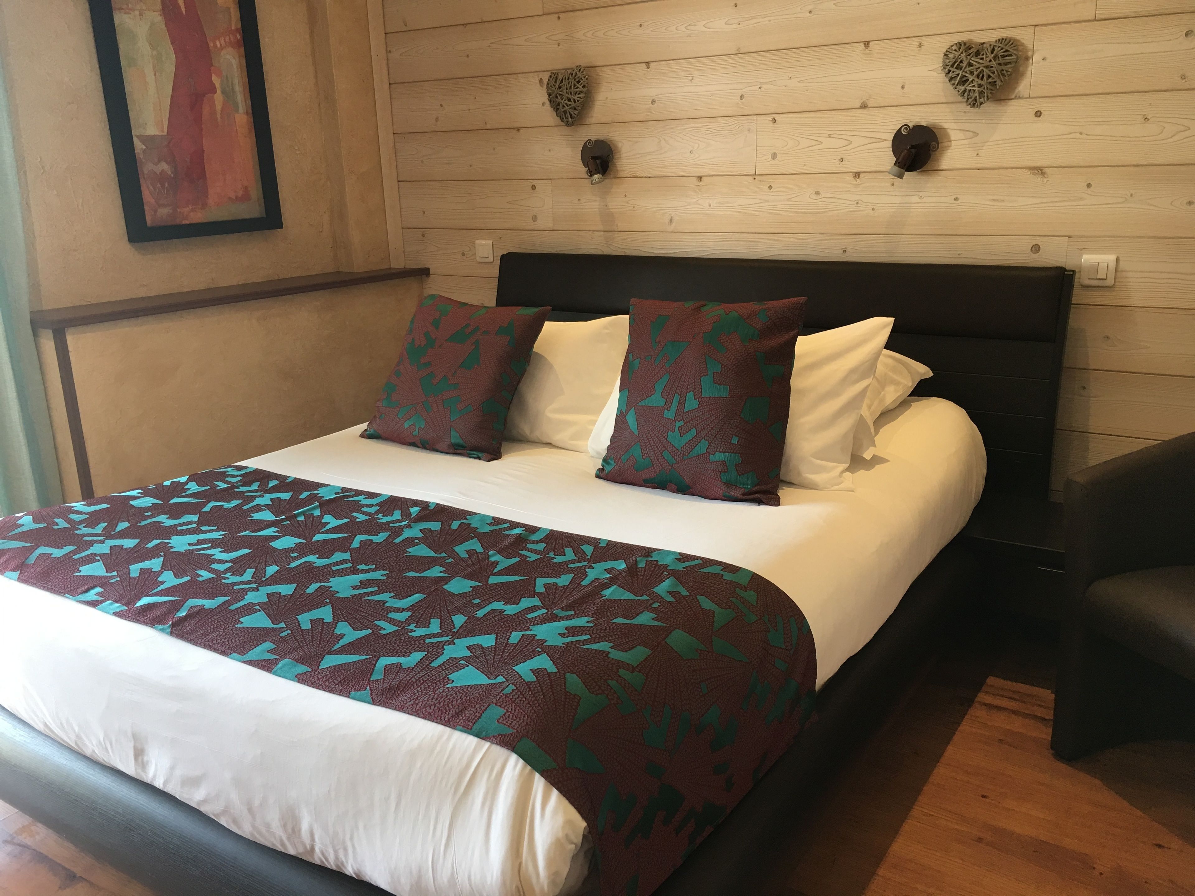A neatly made bed with a patterned bedspread, two pillows with a leaf design, and a wooden headboard.