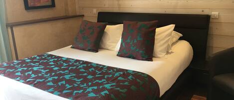 A neatly made bed with a patterned bedspread, two pillows with a leaf design, and a wooden headboard.