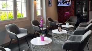 A modern waiting area with grey chairs, round tables, and a television on the wall. - La Bonbonniere, Sure Hotel Collection by Best Western (Talant)