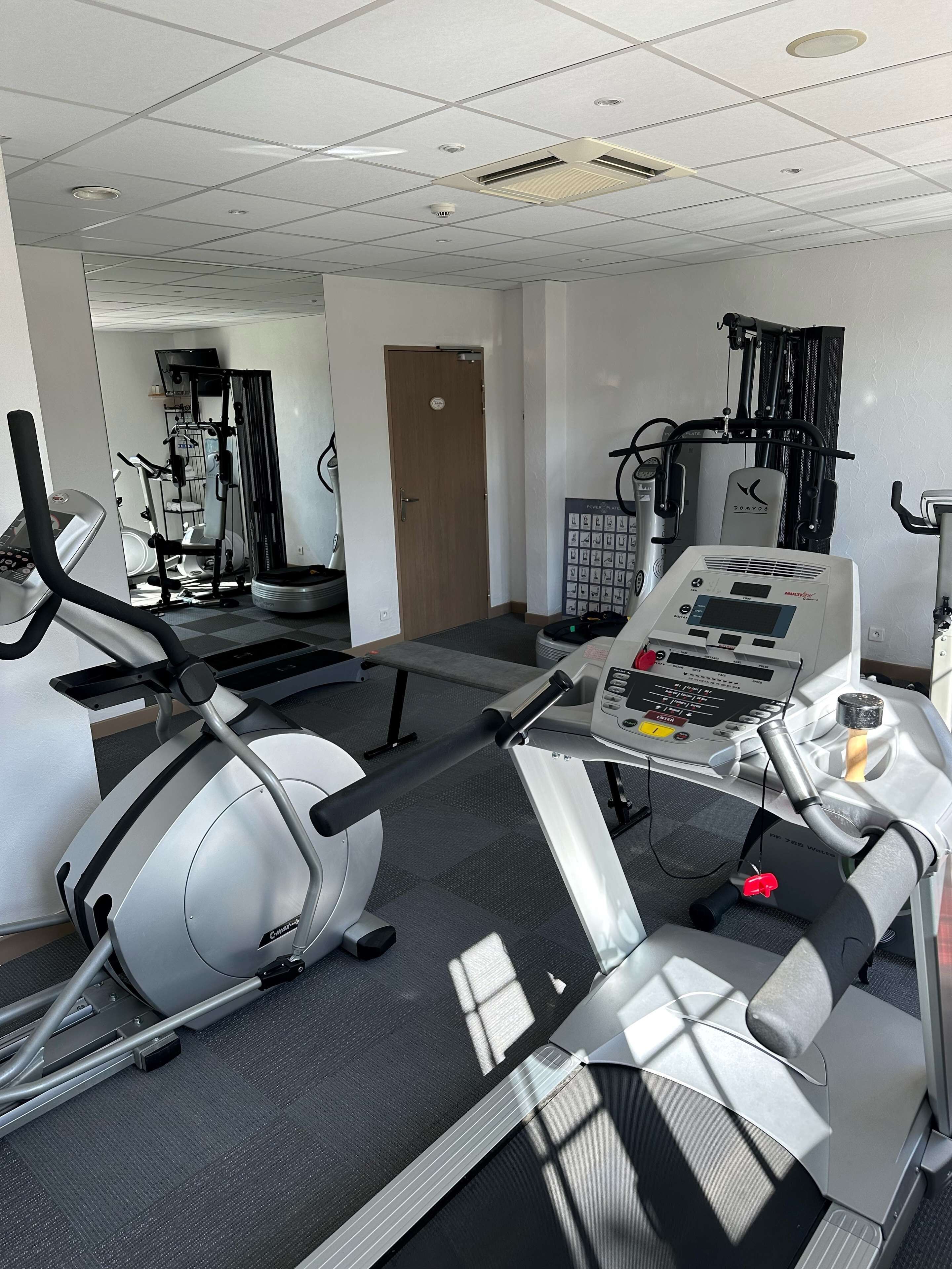 Un gimnasio con máquinas de cardio, equipo de levantamiento de pesas y un panel de control.