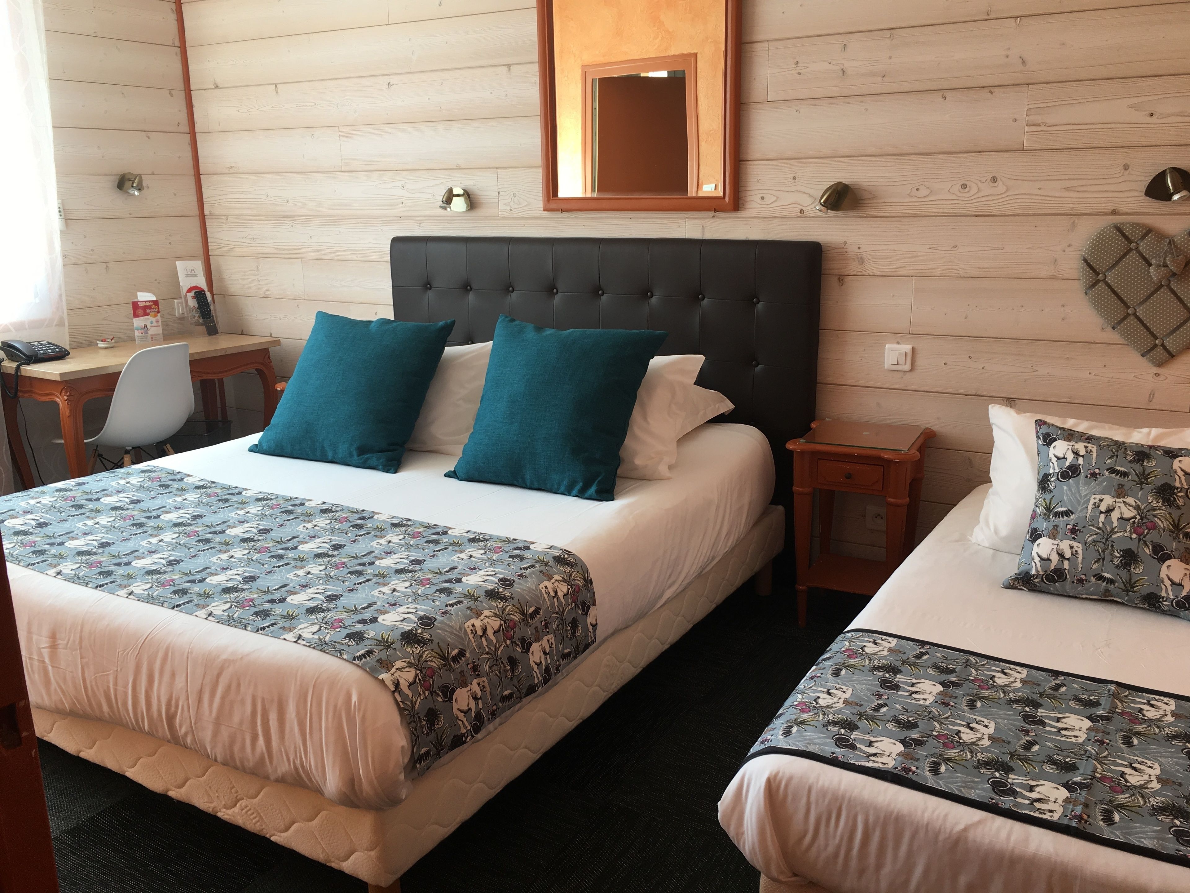A hotel room with a large bed, a smaller bed, a desk, and a mirror on the wall.