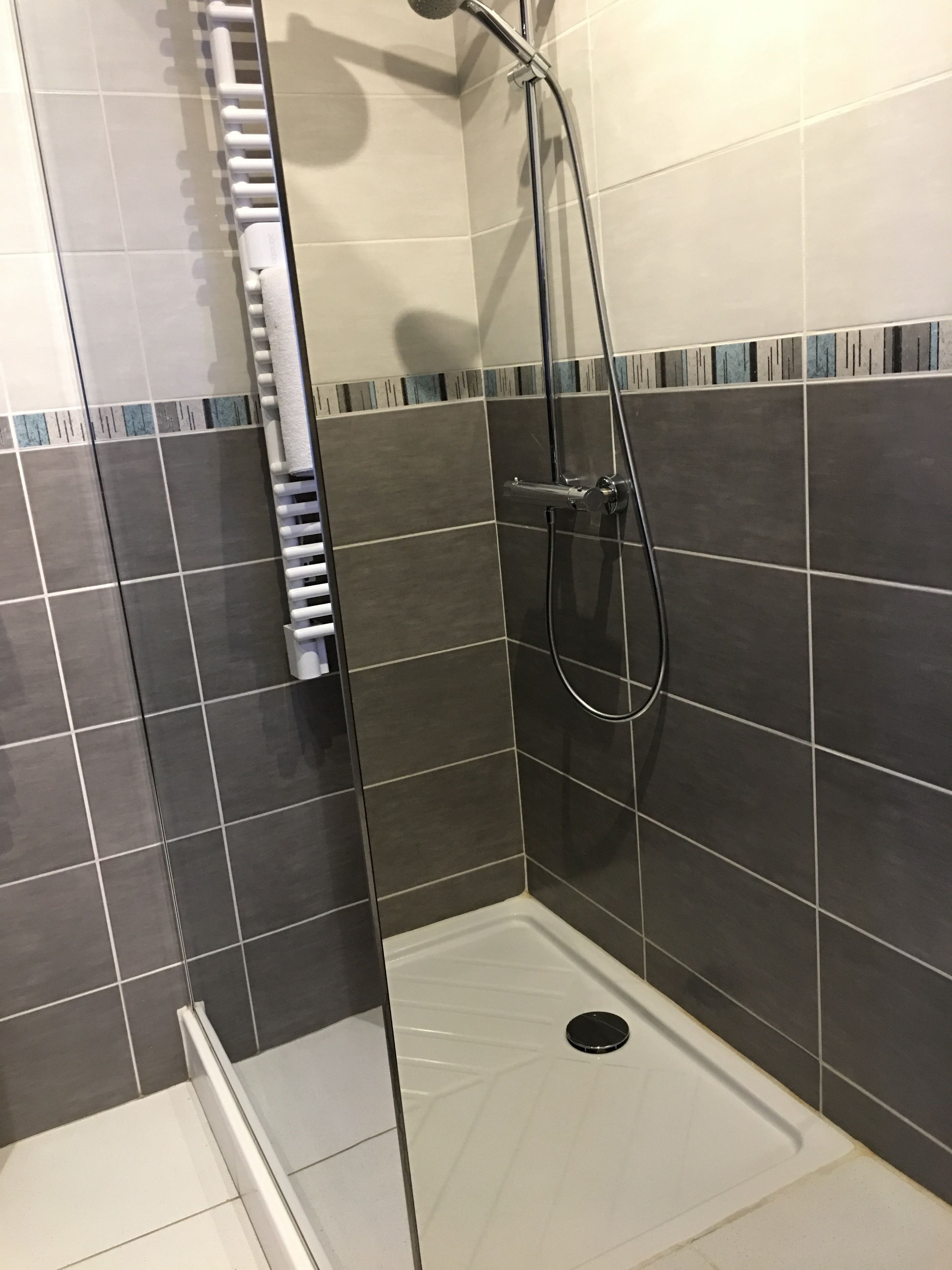 A shower with a glass door, a handheld showerhead, and a towel rack.