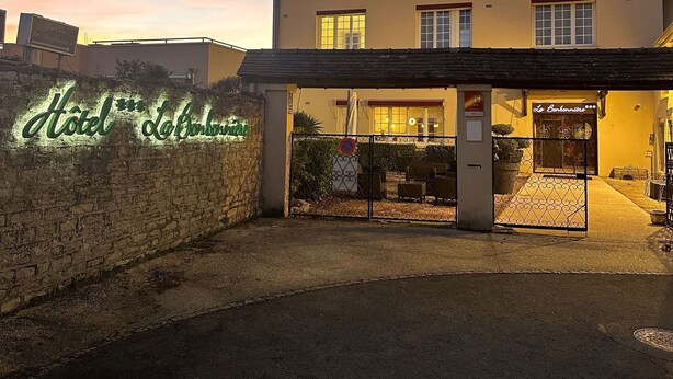 A hotel with a stone wall entrance, a neon sign, and a gated driveway. - La Bonbonniere, Sure Hotel Collection by Best Western (Talant)